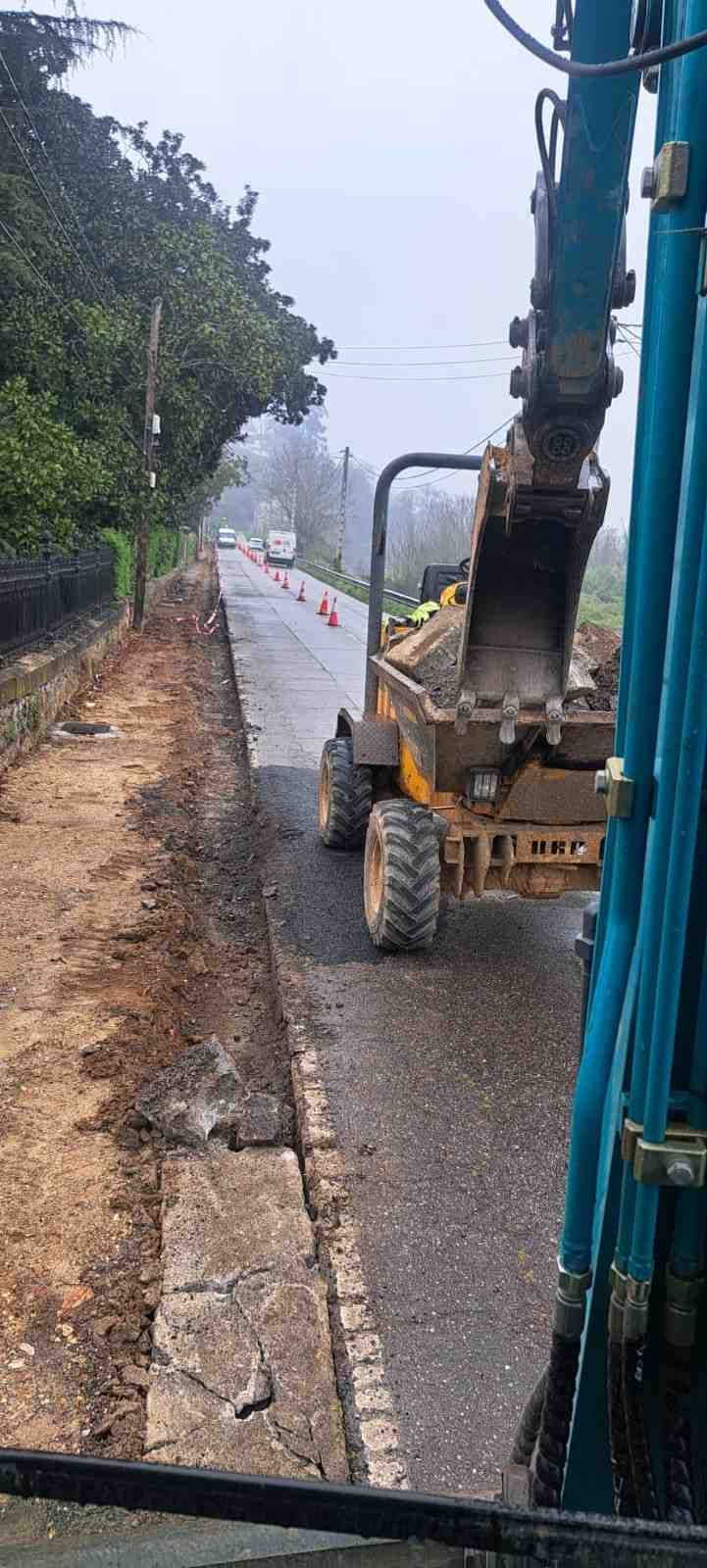 Retroexcavadora trabajando junto a una carretera mojada, excavando a lo largo de un terraplén fangoso.