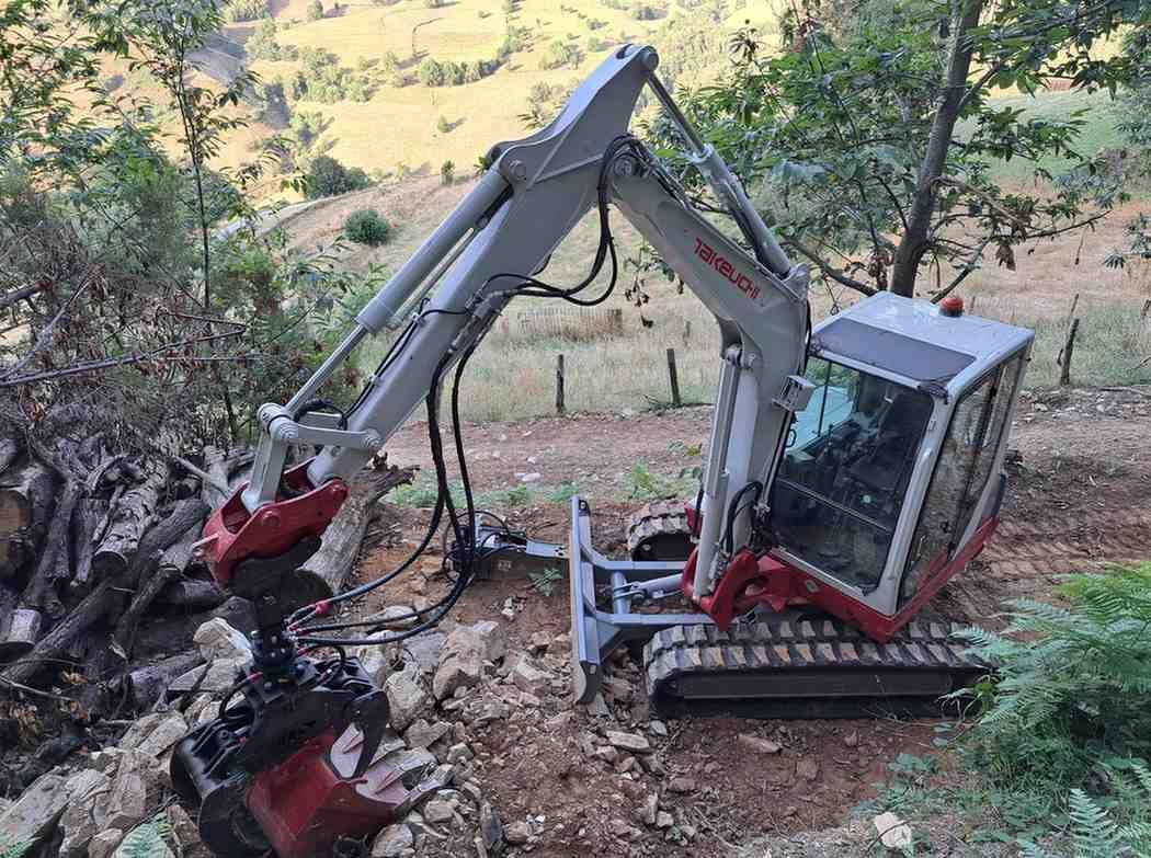 Excavadora volcada de lado en un campo de tierra, con la pluma levantada y la cabina hacia abajo.