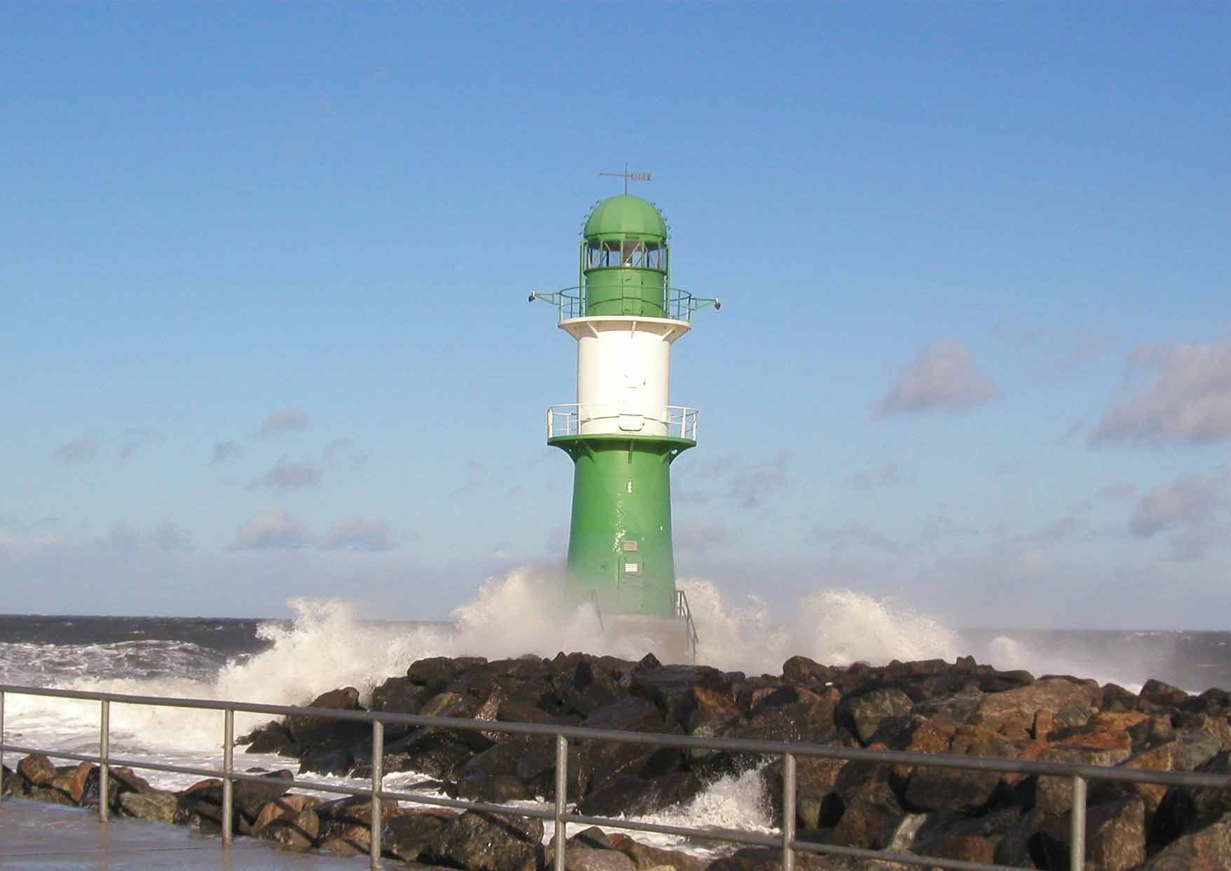 Ein grün-weißer Leuchtturm ist von Wellen umgeben