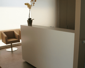 Uma área de recepção moderna com uma mesa branca minimalista, uma pequena orquídea em vaso e uma única cadeira bege.