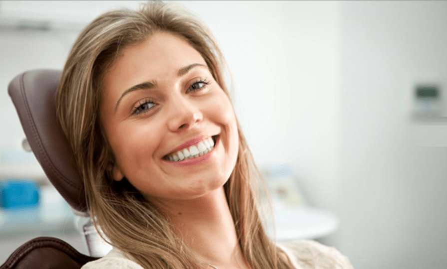 Uma pessoa sorridente sentada em uma cadeira de dentista, olhando para a câmera em um consultório moderno e bem iluminado.
