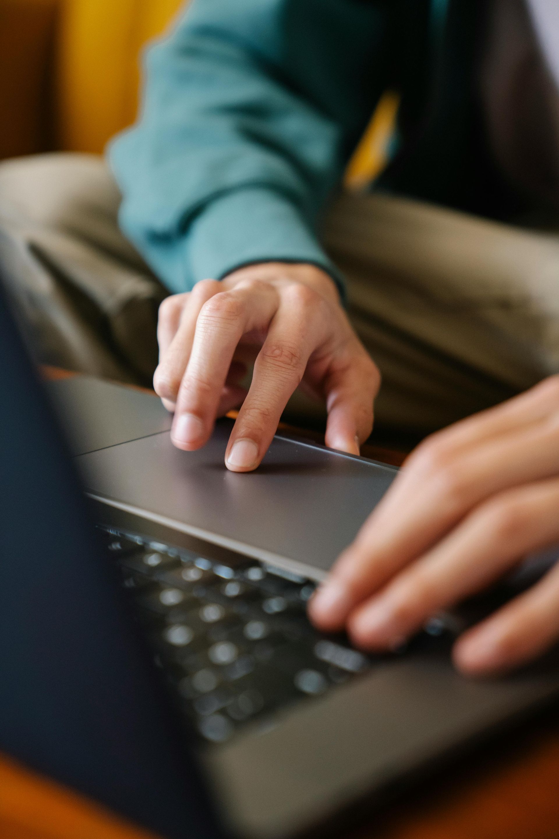 Una persona que lleva un suéter color turquesa utiliza el panel táctil y el teclado de una computadora portátil oscura.