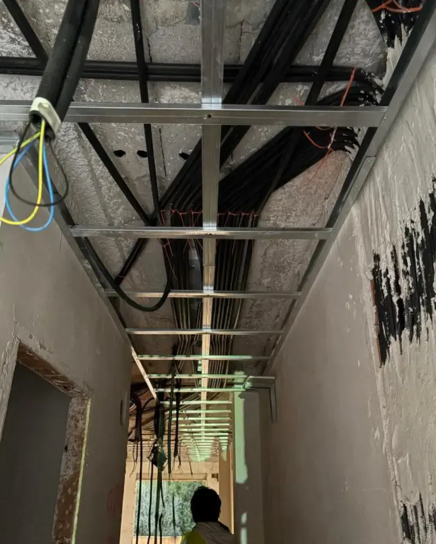 Techo del pasillo con estructura metálica, cableado y aislamiento a la vista. Persona visible al final.