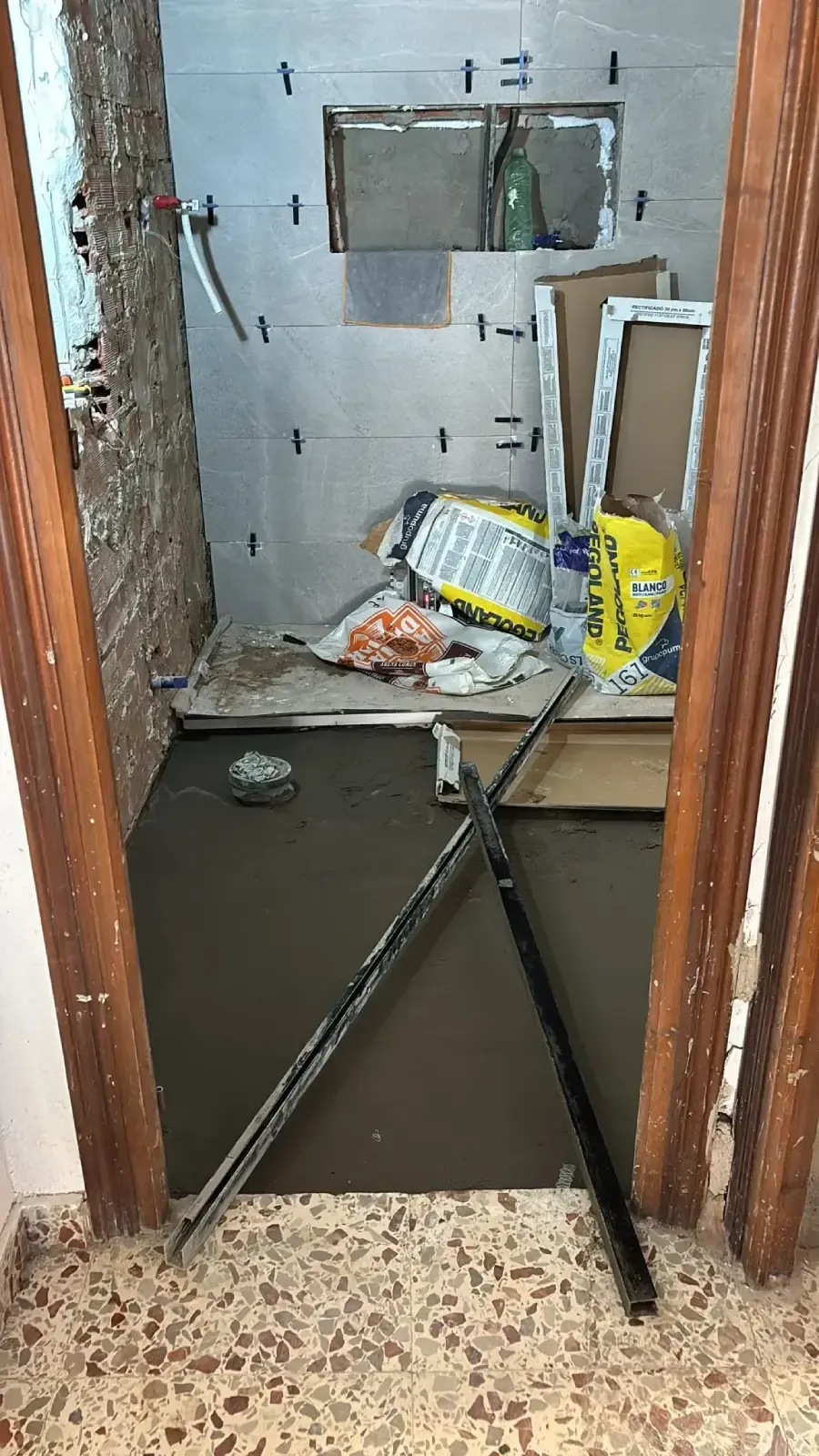 Baño en construcción; las paredes están parcialmente revestidas, el piso es de concreto húmedo