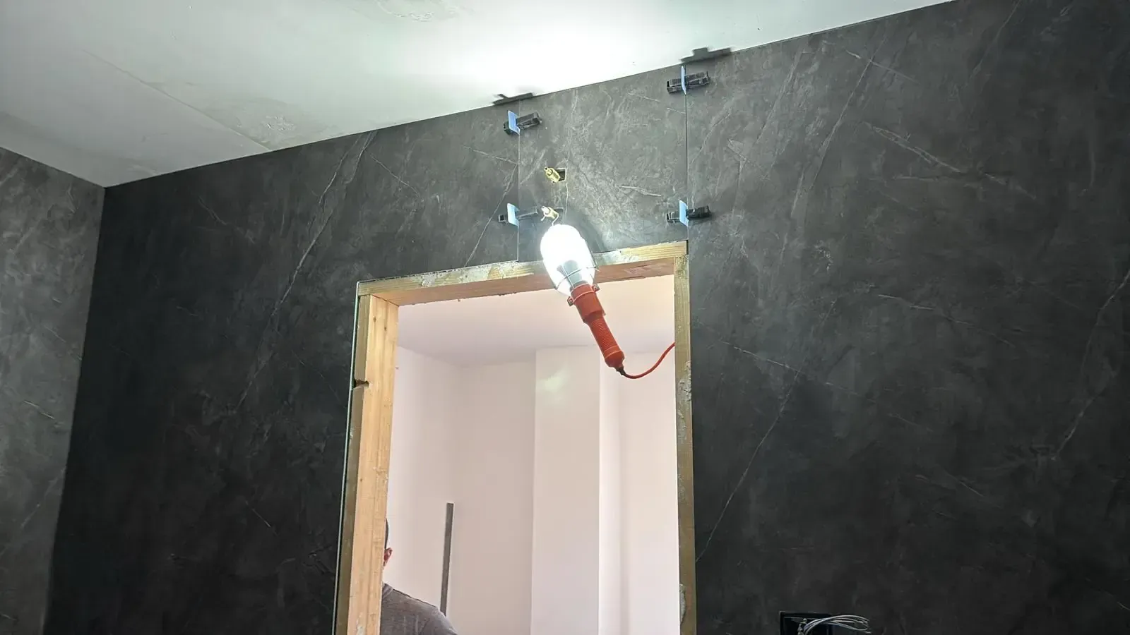Pared oscura con puerta, encima hay una lámpara de trabajo.