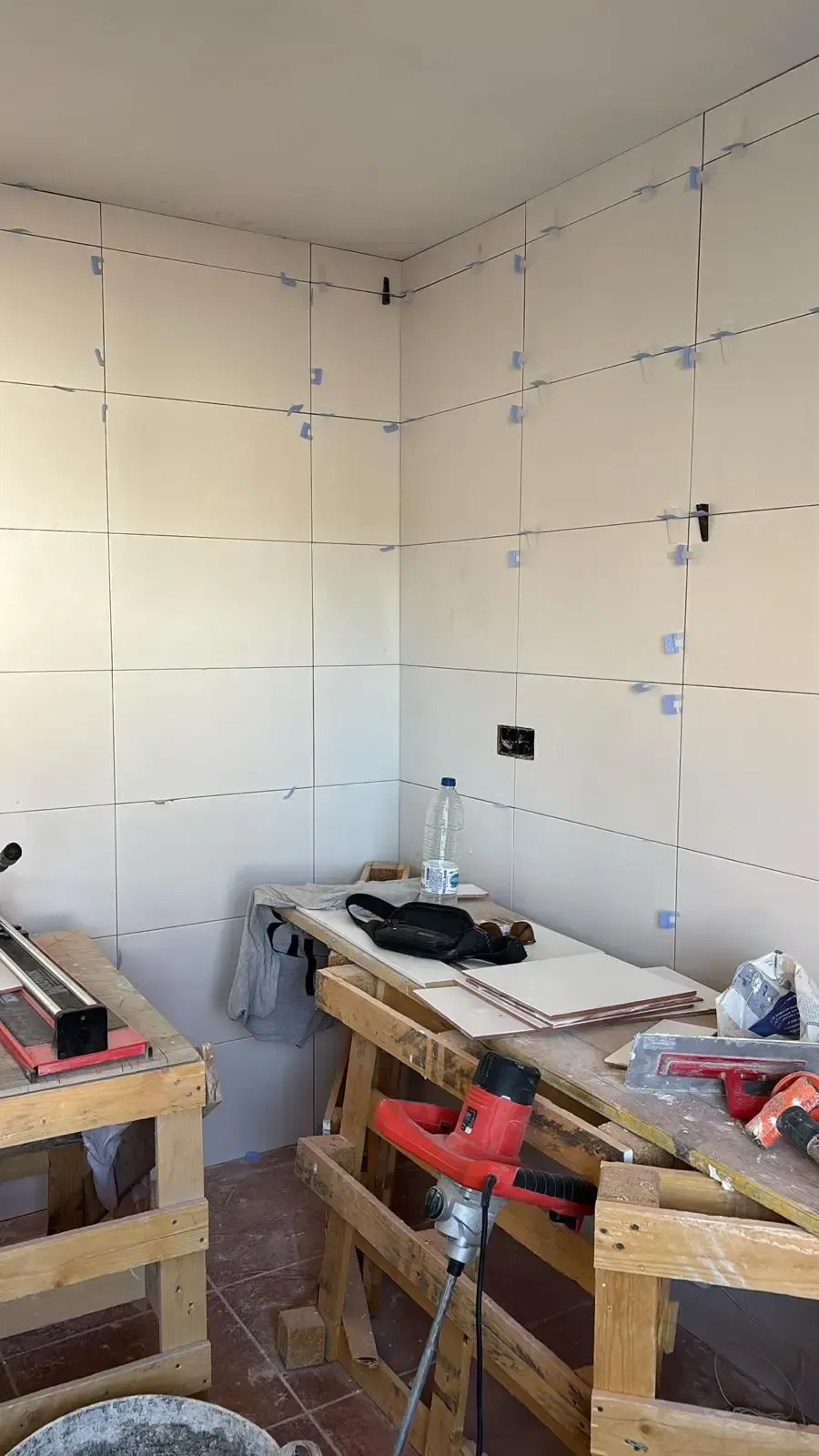 Habitación con paredes de azulejos de color blanquecino, espaciadores de azulejos y herramientas en un banco de trabajo