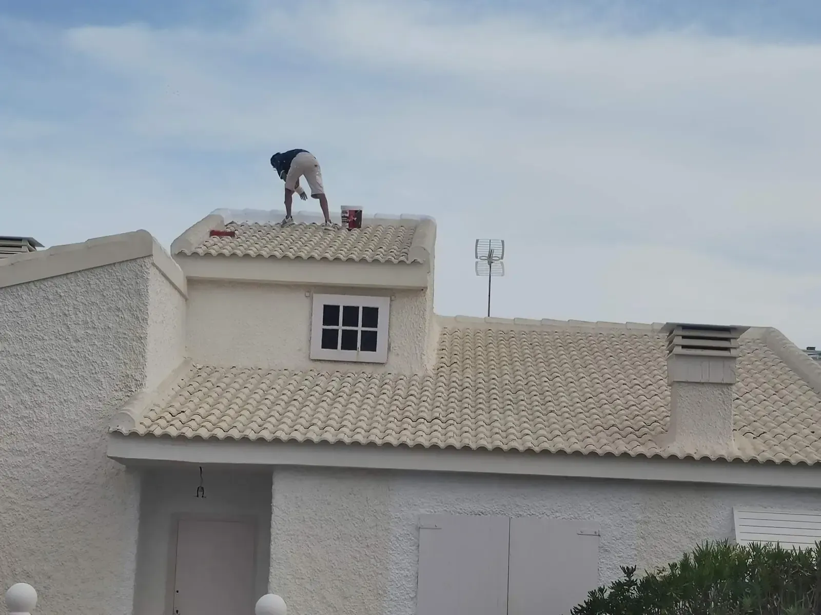 Persona pintando el tejado de una casa blanca bajo un cielo nublado.