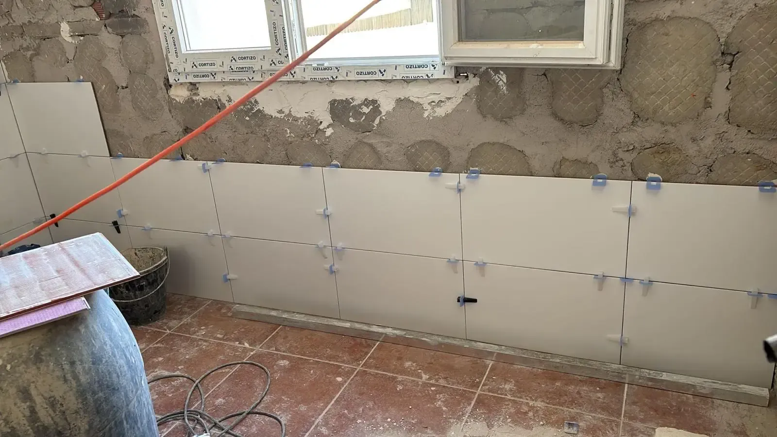 Azulejos blancos que se instalan en una pared, con espaciadores, en una habitación con paredes de piedra