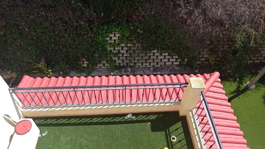 Vista desde arriba de un techo de tejas rojas con una barandilla de metal negro, césped verde