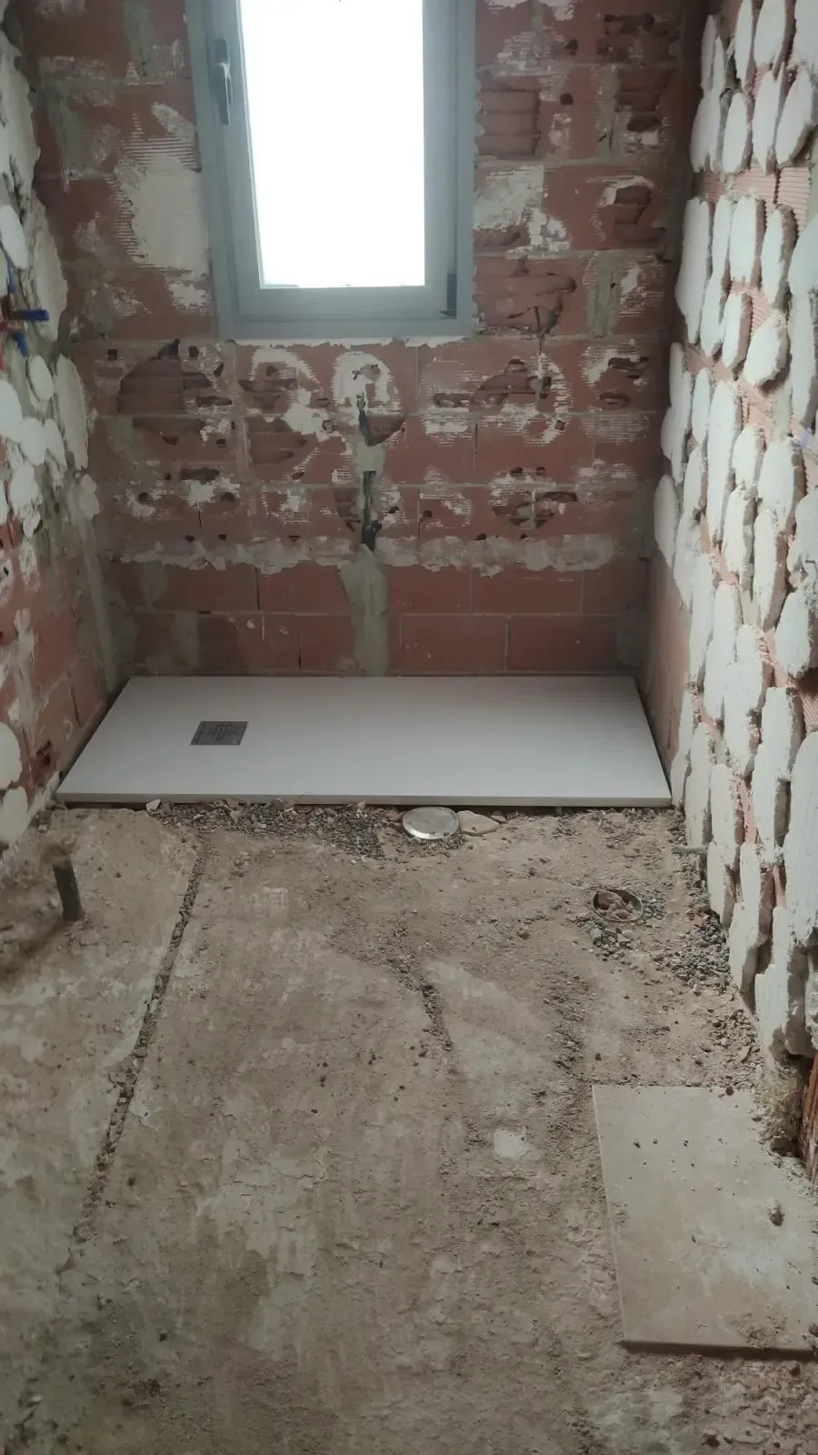 Baño en construcción con base de ducha instalada y paredes de ladrillo.