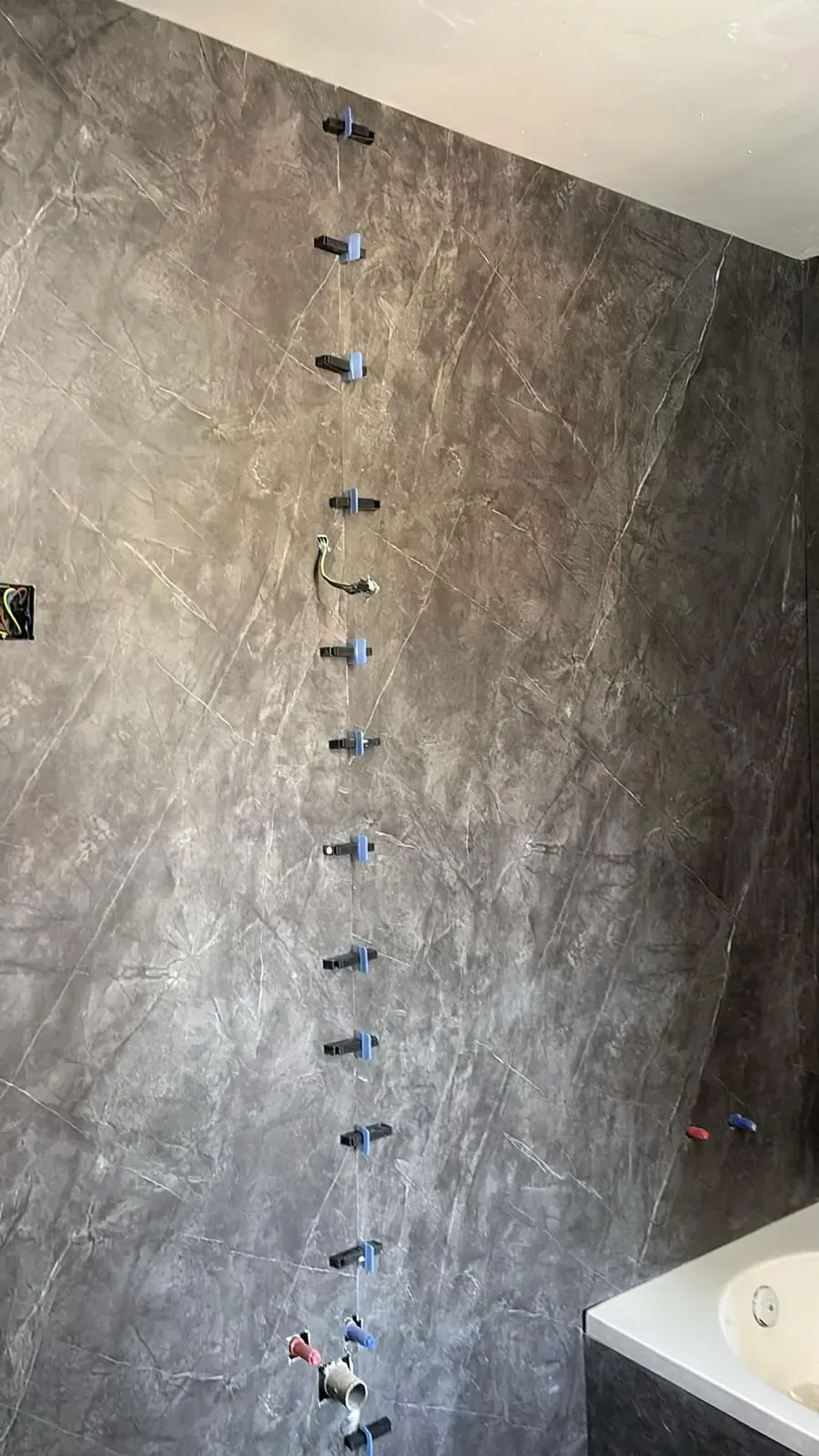 Pared de ducha con azulejos de color gris oscuro con montantes adjuntos, cerca de una bañera blanca.