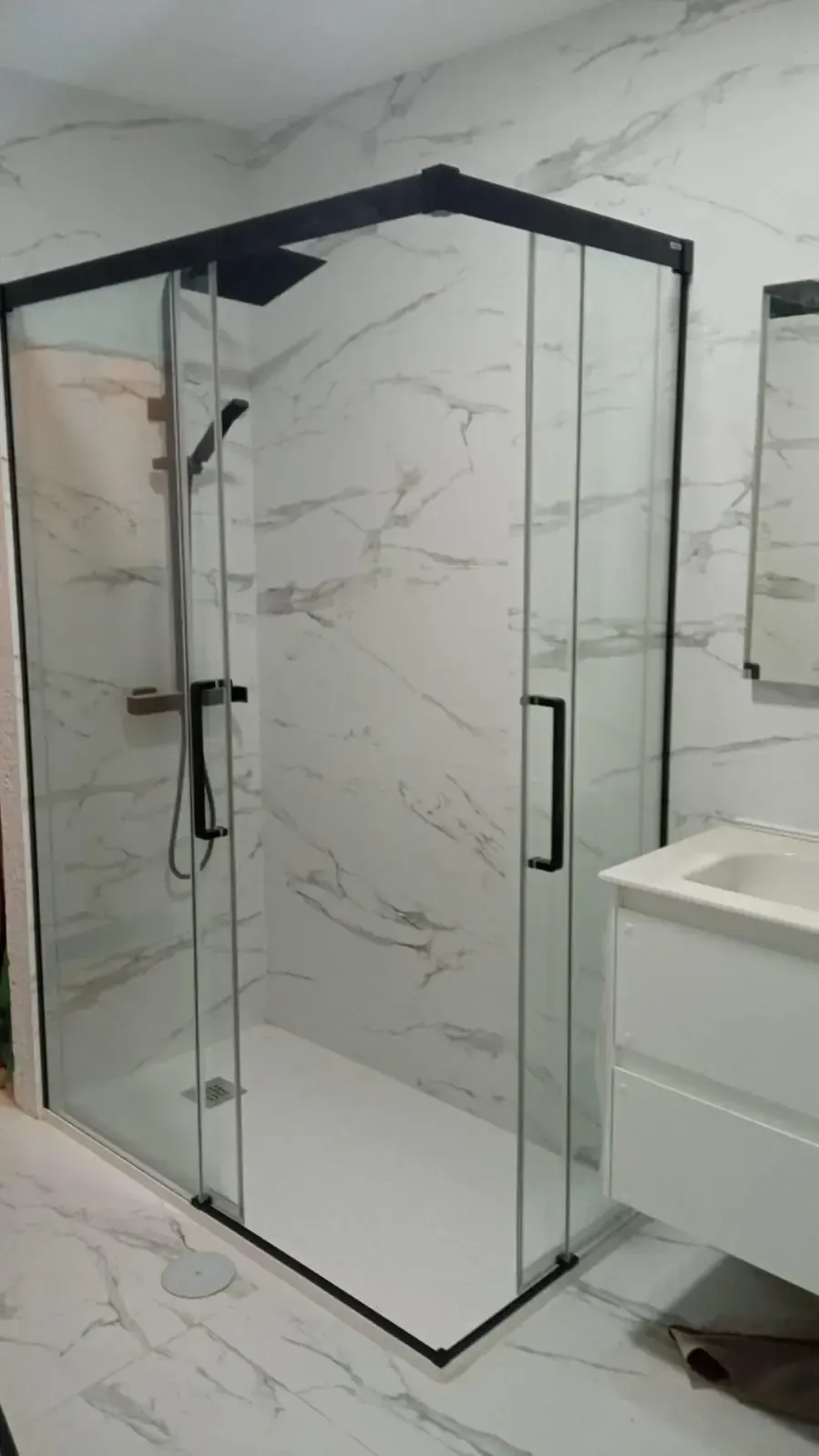 Baño moderno con mampara de ducha de cristal y paredes revestidas con efecto mármol.