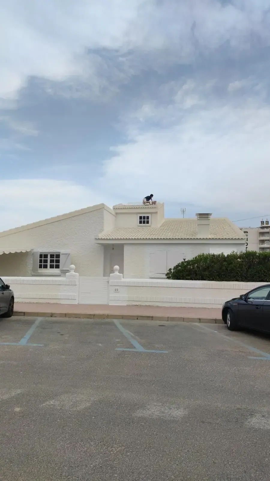 Edificio de estuco blanco con techo inclinado, cerca de un estacionamiento y un cielo nublado.