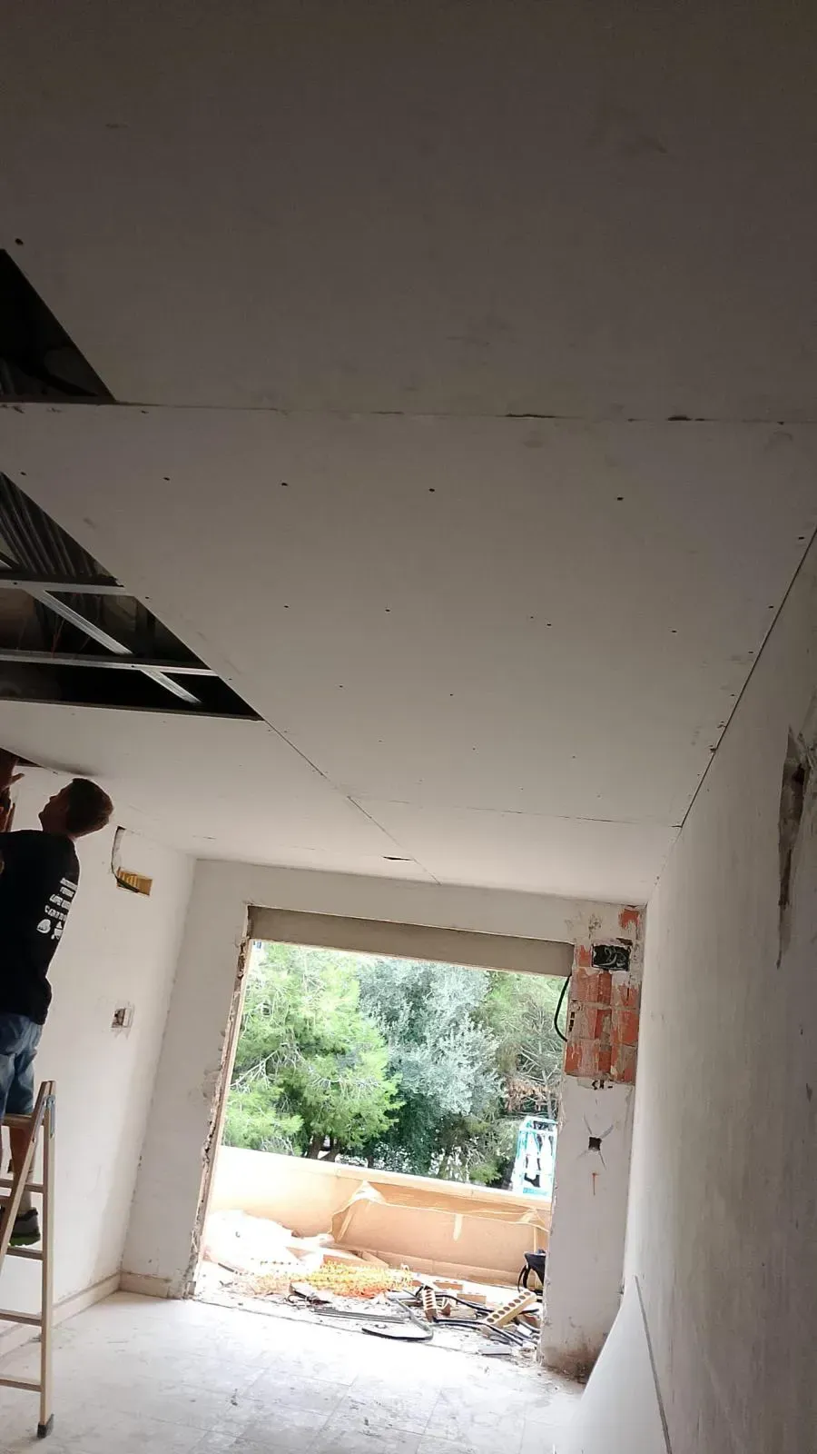 Hombre instalando paneles de yeso en el techo de una habitación con una puerta abierta.