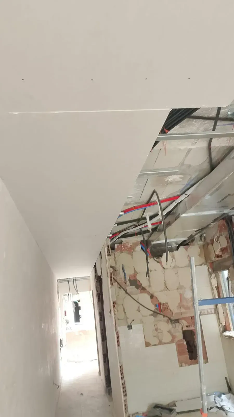 Pasillo en construcción, con paneles de yeso parcialmente instalados. Tuberías y cableado visibles en el techo.