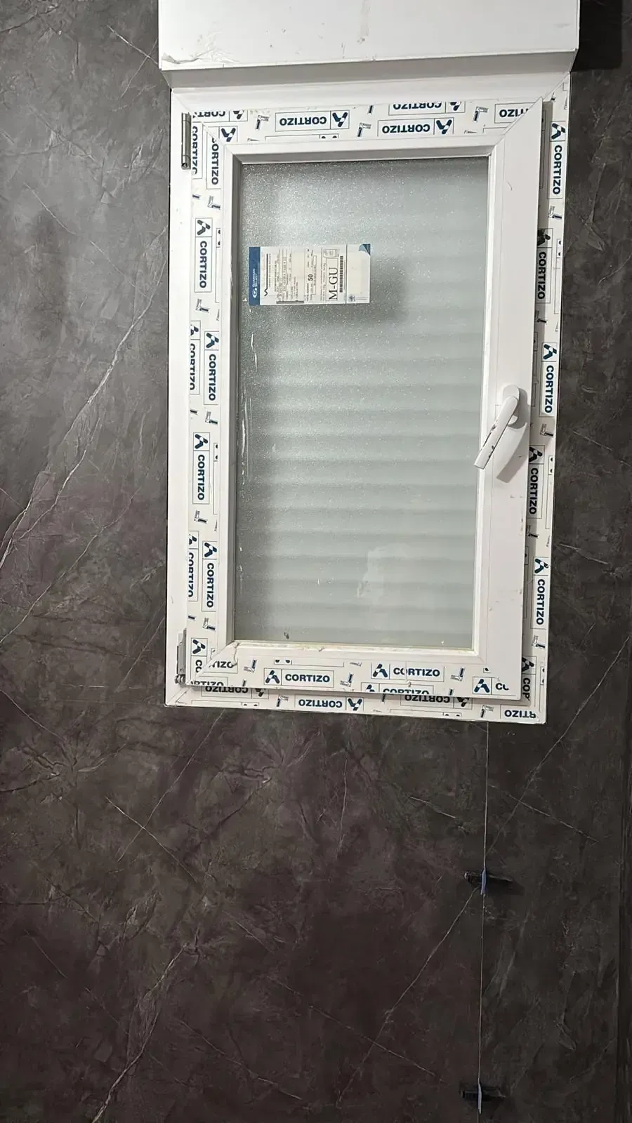 Ventana con marco blanco y panel translúcido sobre una pared gris texturizada.