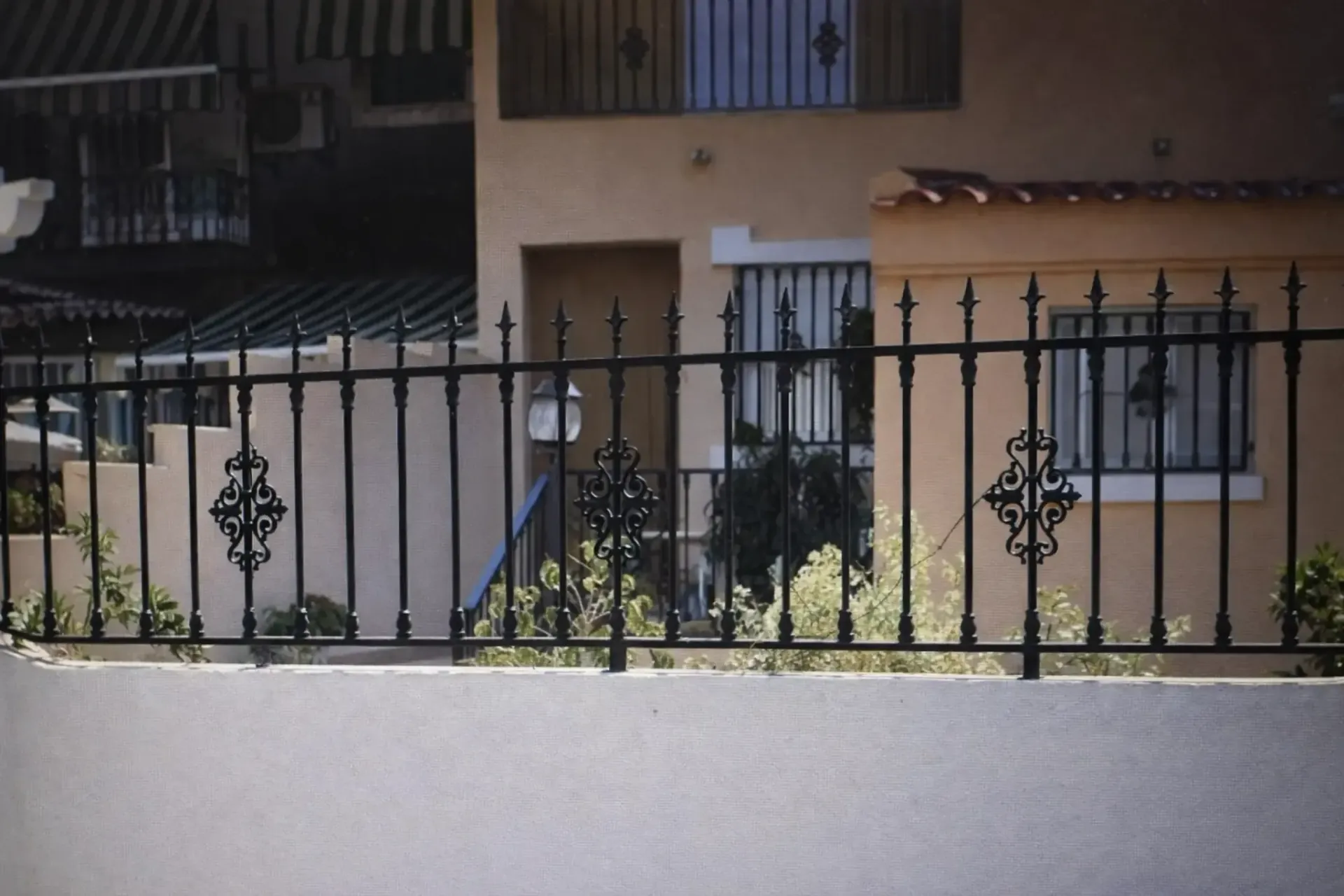 Valla de hierro forjado negro delante de un edificio de color canela con ventanas enrejadas.