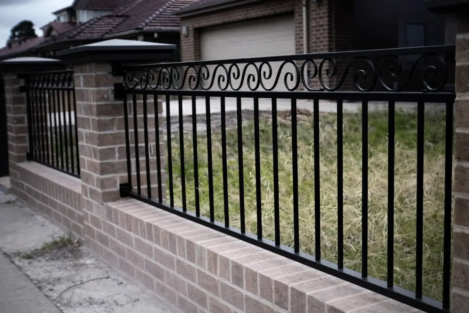 Valla de hierro forjado negro sobre una pared de ladrillos frente a césped verde