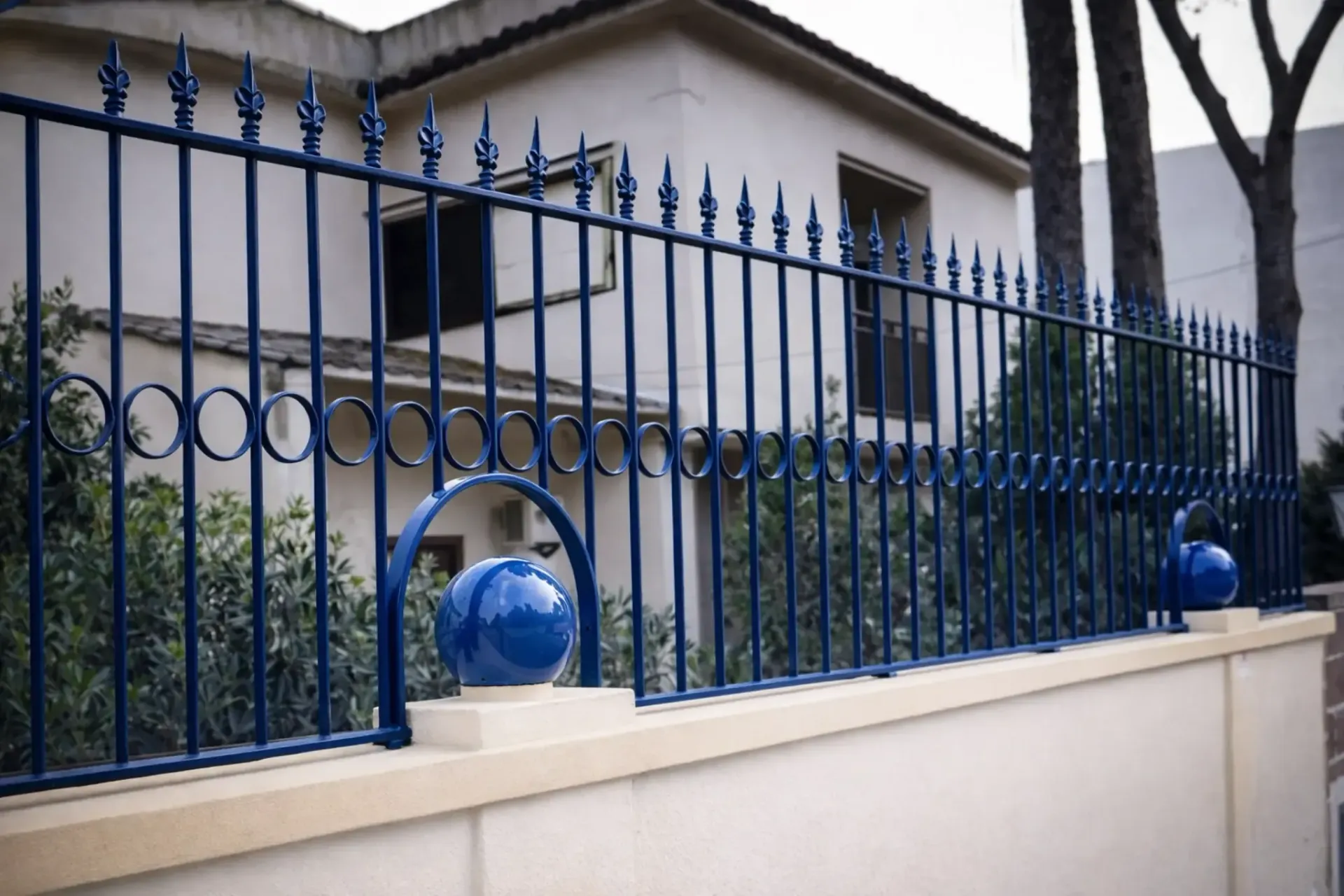 Valla de hierro forjado azul sobre una pared de color crema, frente a una casa.