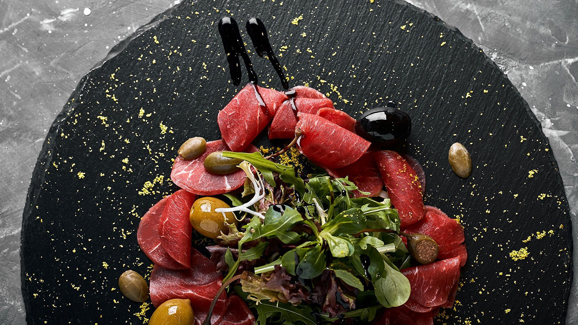 ein schwarzer Teller mit einem Salat aus Fleisch und Oliven