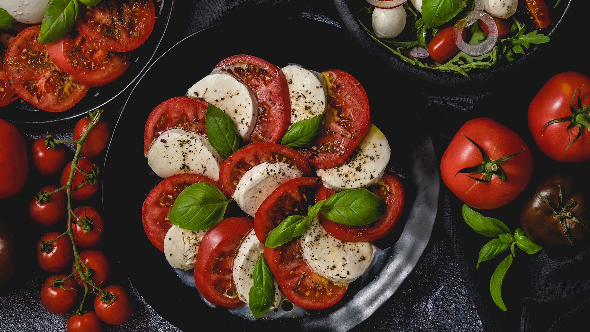 ein Salat mit Tomaten und Mozzarella auf einem schwarzen Teller