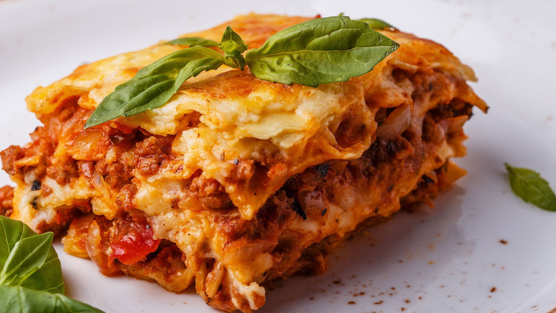 ein Stück lasagne mit basilikumblättern auf einem weißen teller