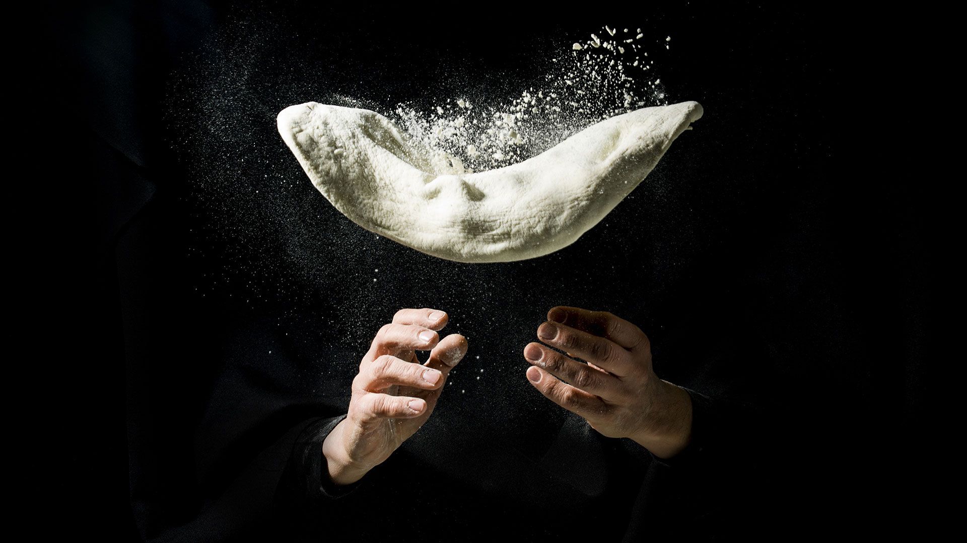 eine Person wirft einen Brötchenteig in die Luft