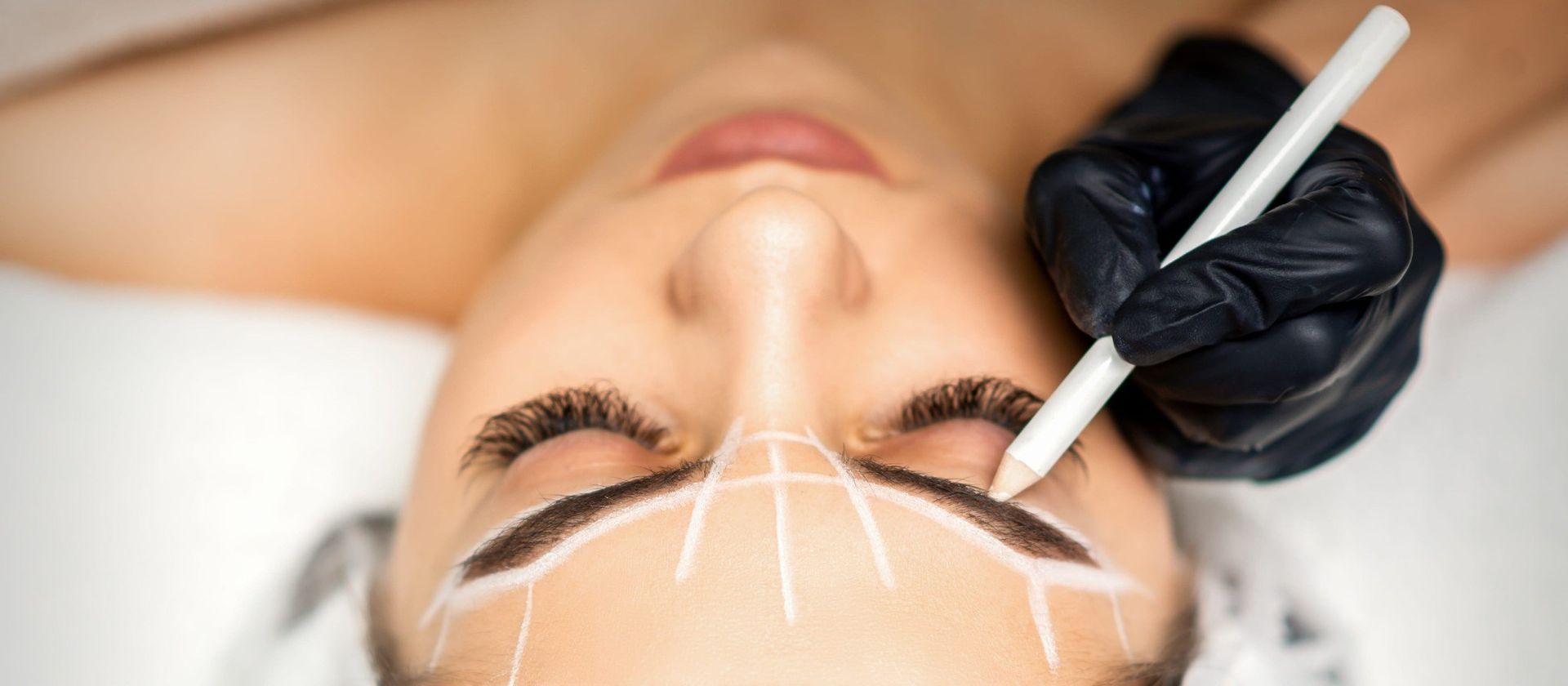 Esteticista aplicando un tratamiento de cejas con marcas blancas en el rostro de una clienta.