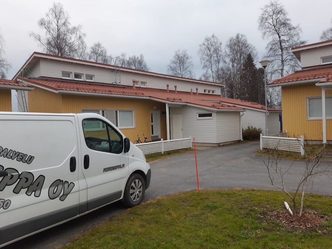 Valkoinen pakettiauto pysäköitynä keltaisten rakennusten viereen lumisella sisäpihalla harmaan taivaan alla