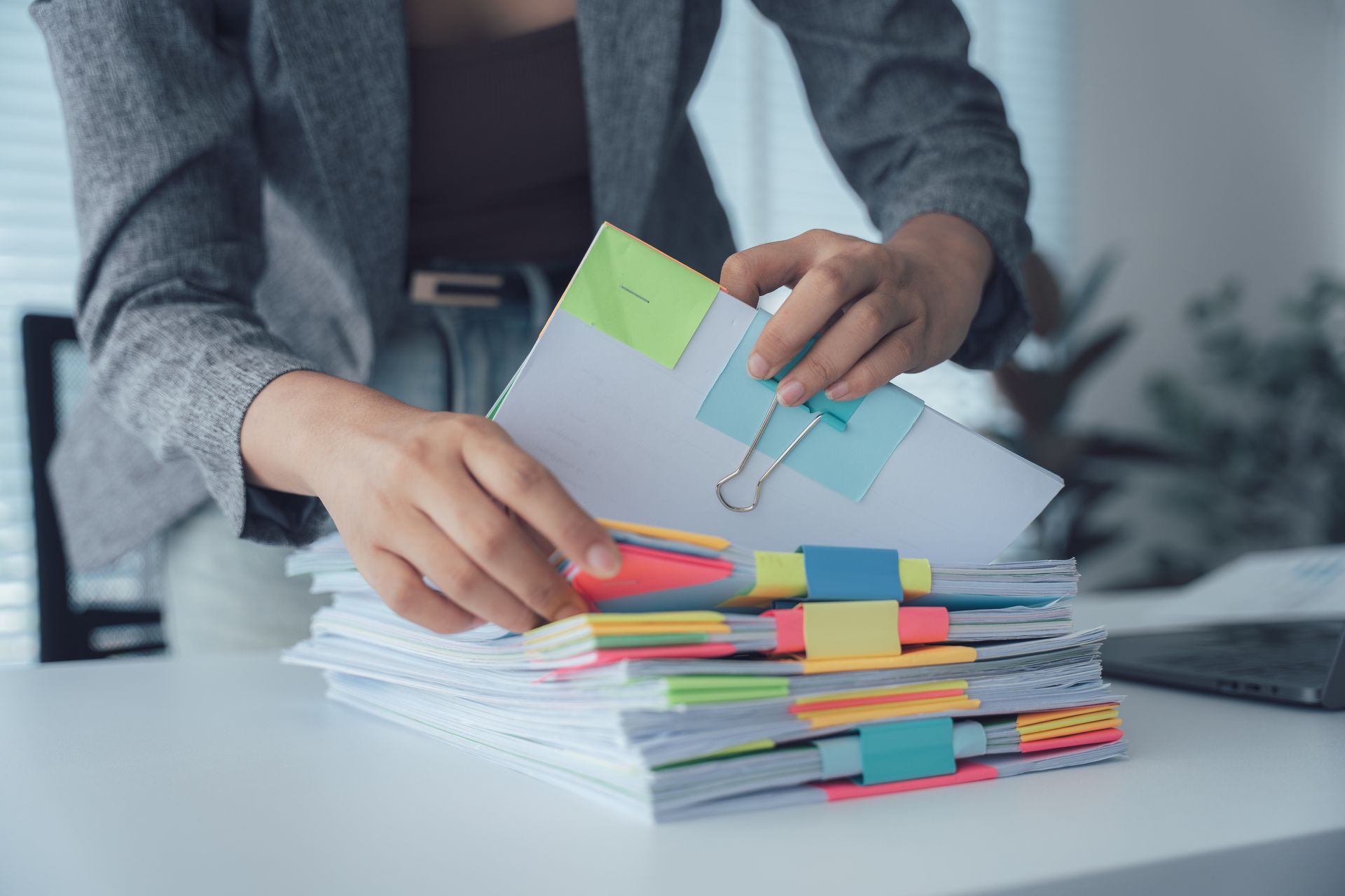 Une personne range une pile de papiers sur un bureau à l'aide de post-it et de pinces à reliure.