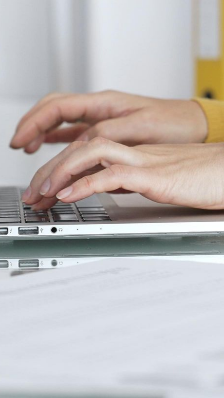 Gros plan sur des mains tapant sur un ordinateur portable. On aperçoit la manche jaune d'un pull.