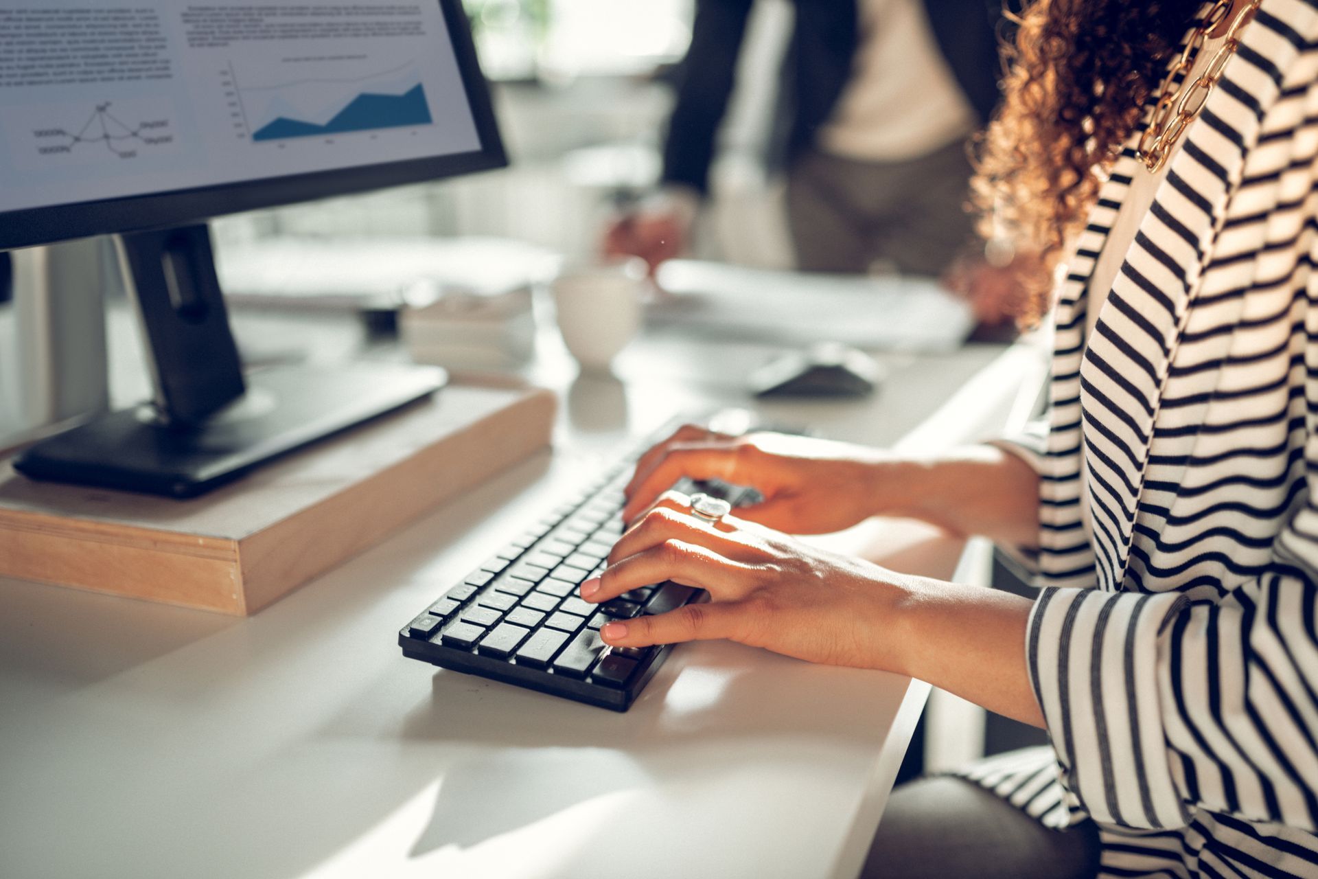 Femme tapant au clavier, regardant un écran d'ordinateur affichant des graphiques. Bureau blanc, environnement de bureau.