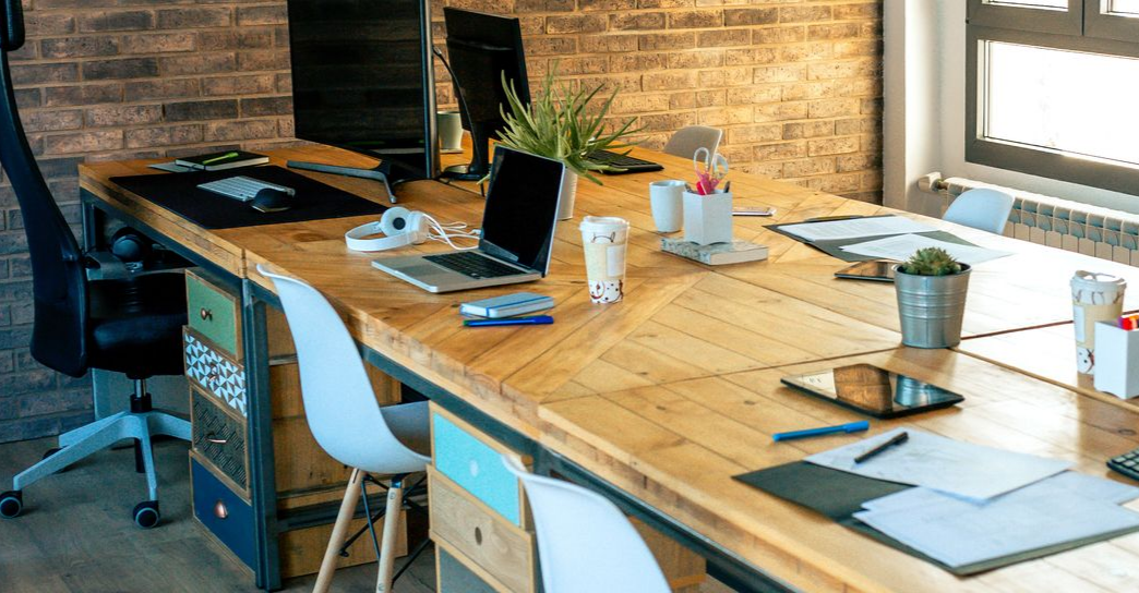 Long bureau en bois avec fournitures de bureau, ordinateurs et chaises dans un bureau moderne.