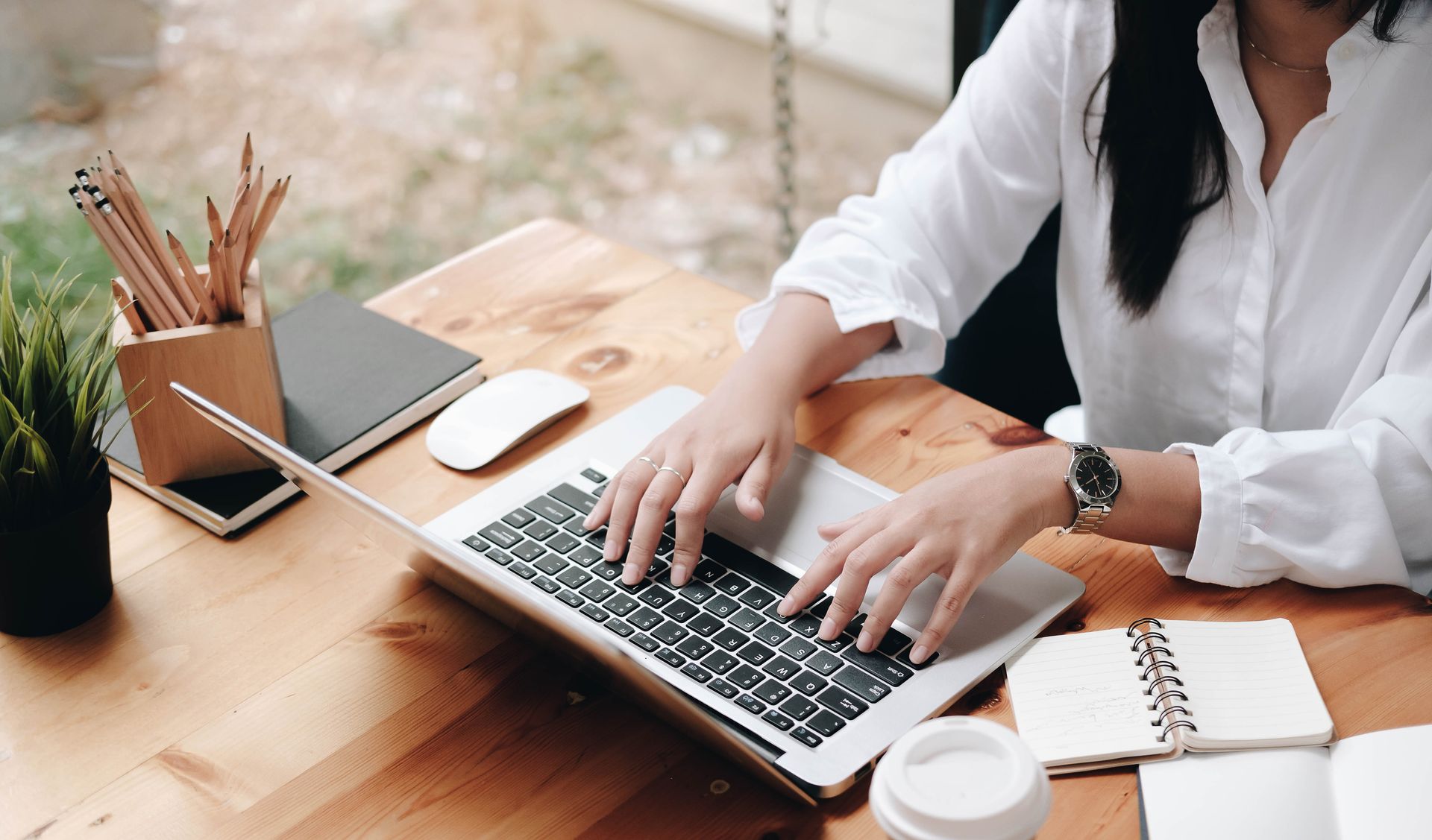 Une femme tape sur un ordinateur portable à un bureau en bois, entourée de fournitures de bureau.