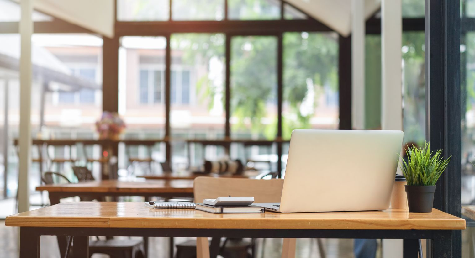 Ordinateur portable et plante sur un bureau en bois à l'intérieur d'un café lumineux, arrière-plan flou avec des tables.
