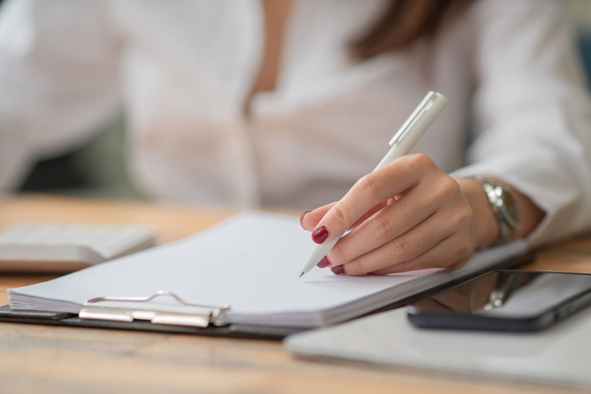 Femme en chemise blanche écrivant sur un bloc-notes avec un stylo à un bureau.