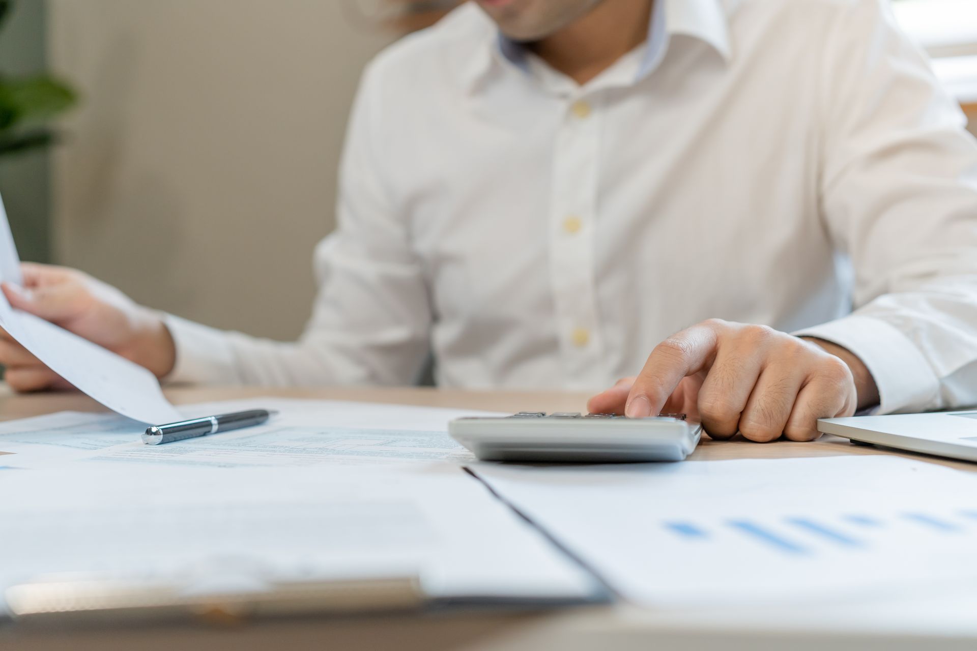 Un homme en chemise blanche effectue des calculs financiers avec une calculatrice, entouré de papiers sur un bureau.