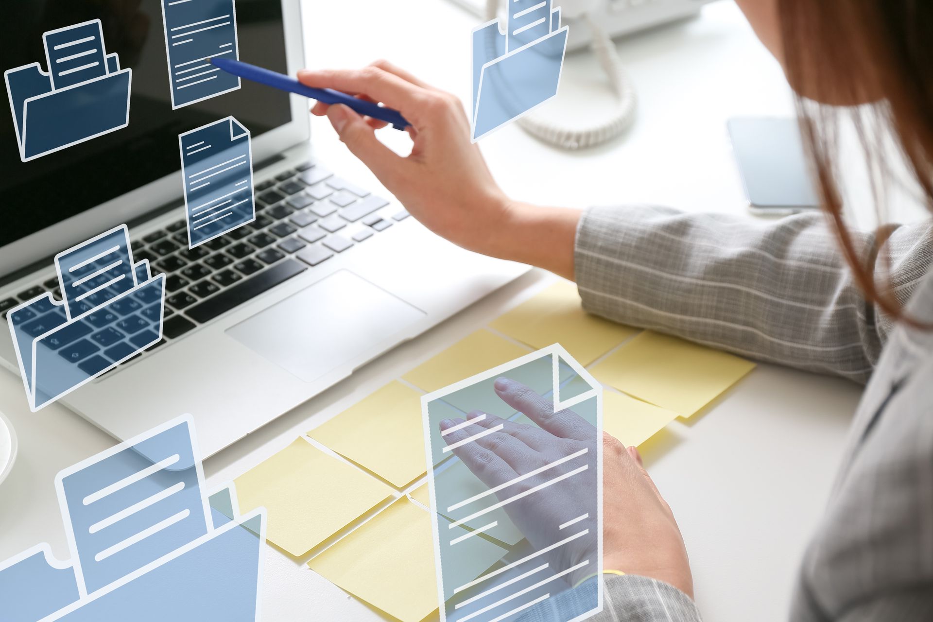 Femme pointant du doigt l'écran d'un ordinateur portable avec des icônes de documents superposées ; bureau avec des notes adhésives.