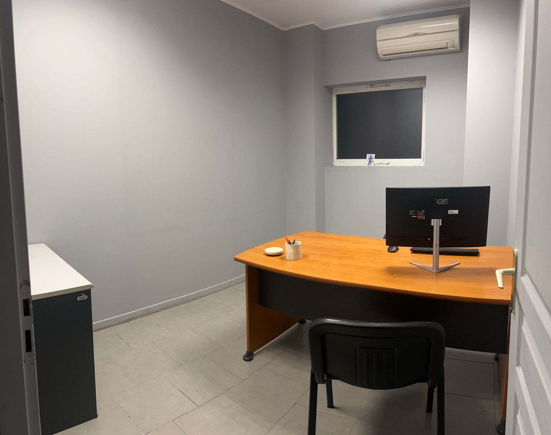 Ordinateur portable, carnet et plante en pot sur une table en bois dans un café, avec des tables et des fenêtres floues en arrière-plan.