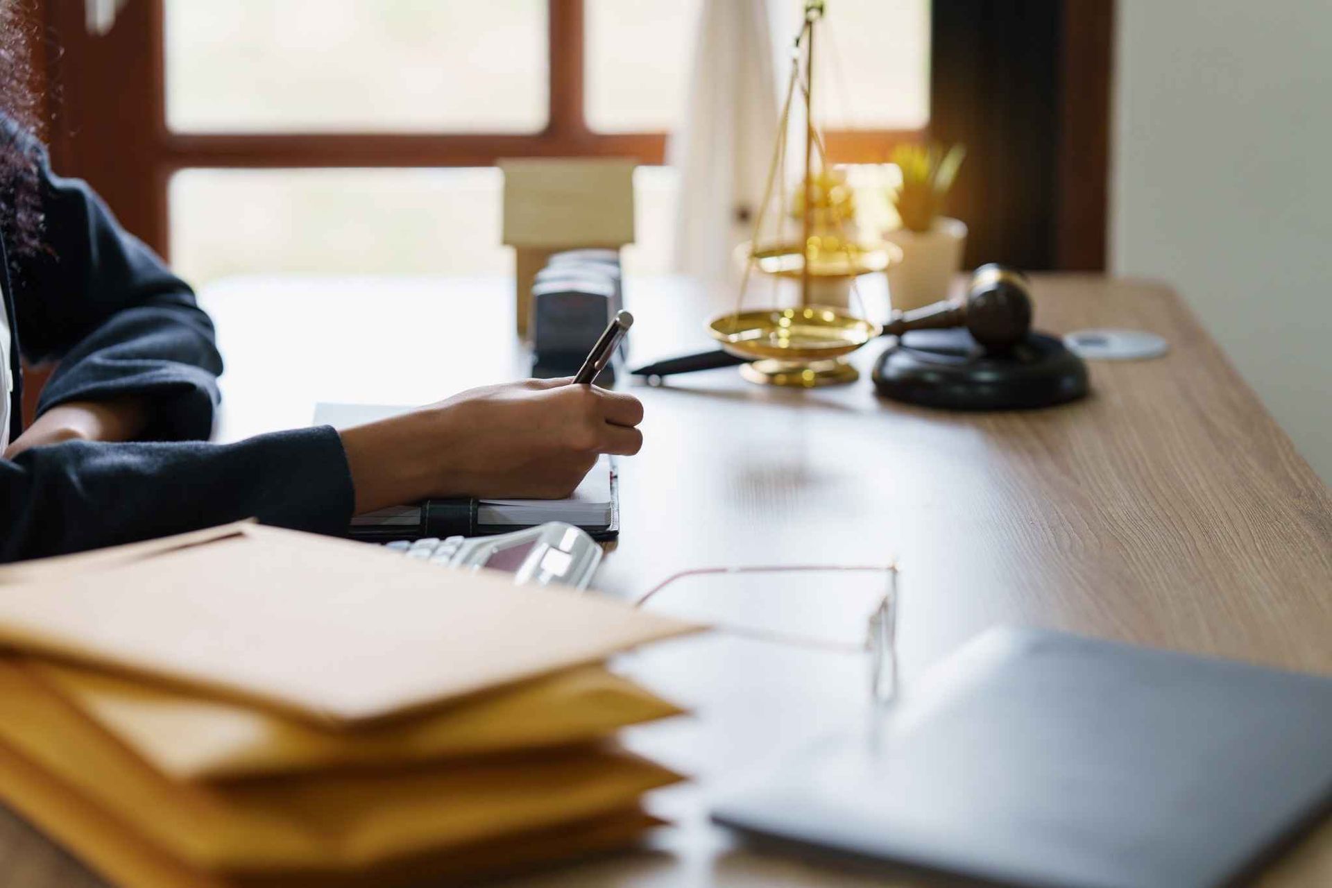 Persona escribiendo en un escritorio con balanza legal, mazo y documentos.