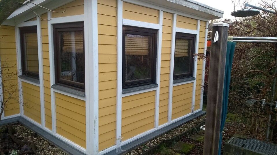 Ein kleines gelb-weißes Haus mit einer Dusche daneben.