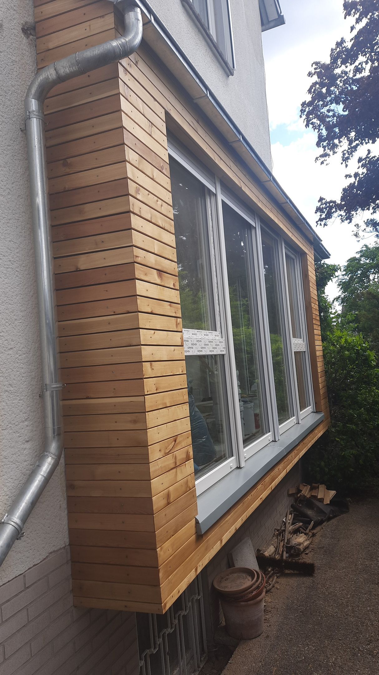 Eine Holzwand mit einem Fenster und einem Abflussrohr an der Seite eines Hauses.