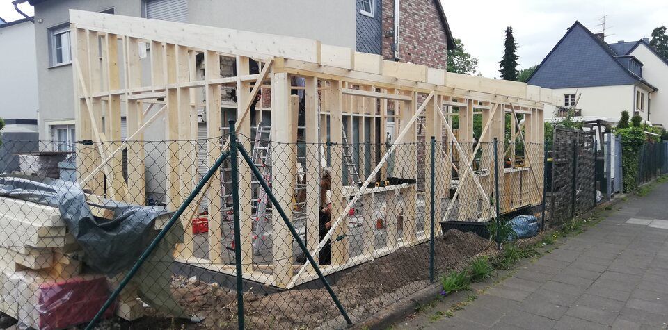 Neben einem Maschendrahtzaun wird eine Holzkonstruktion errichtet