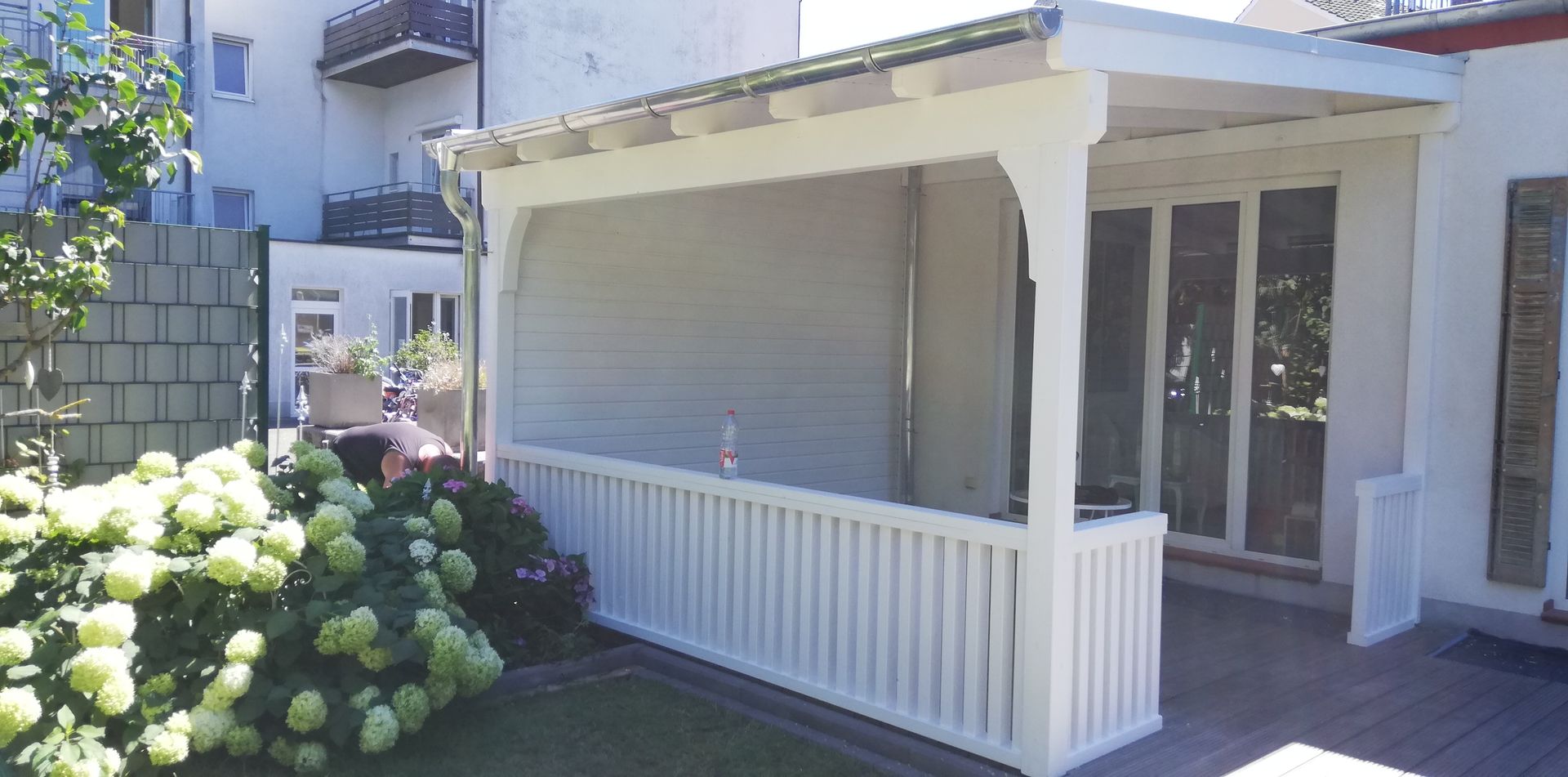 Im Hinterhof eines Hauses steht eine weiße Pergola.