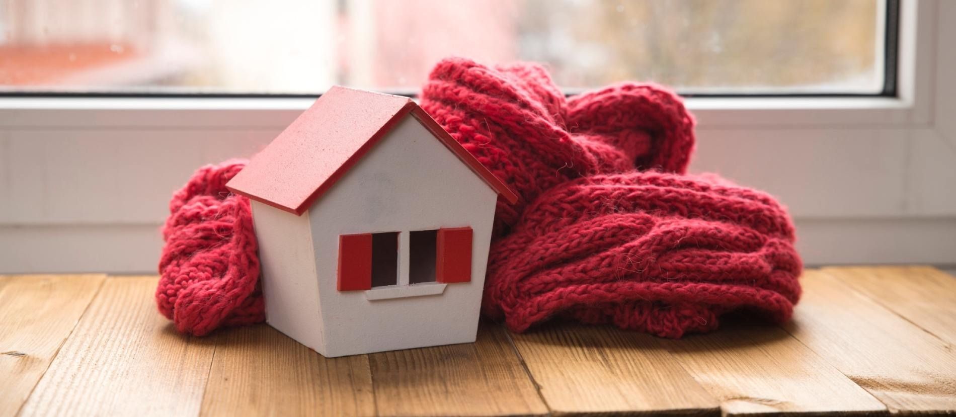 Una pequeña casa está envuelta en un pañuelo rojo sobre una mesa de madera.