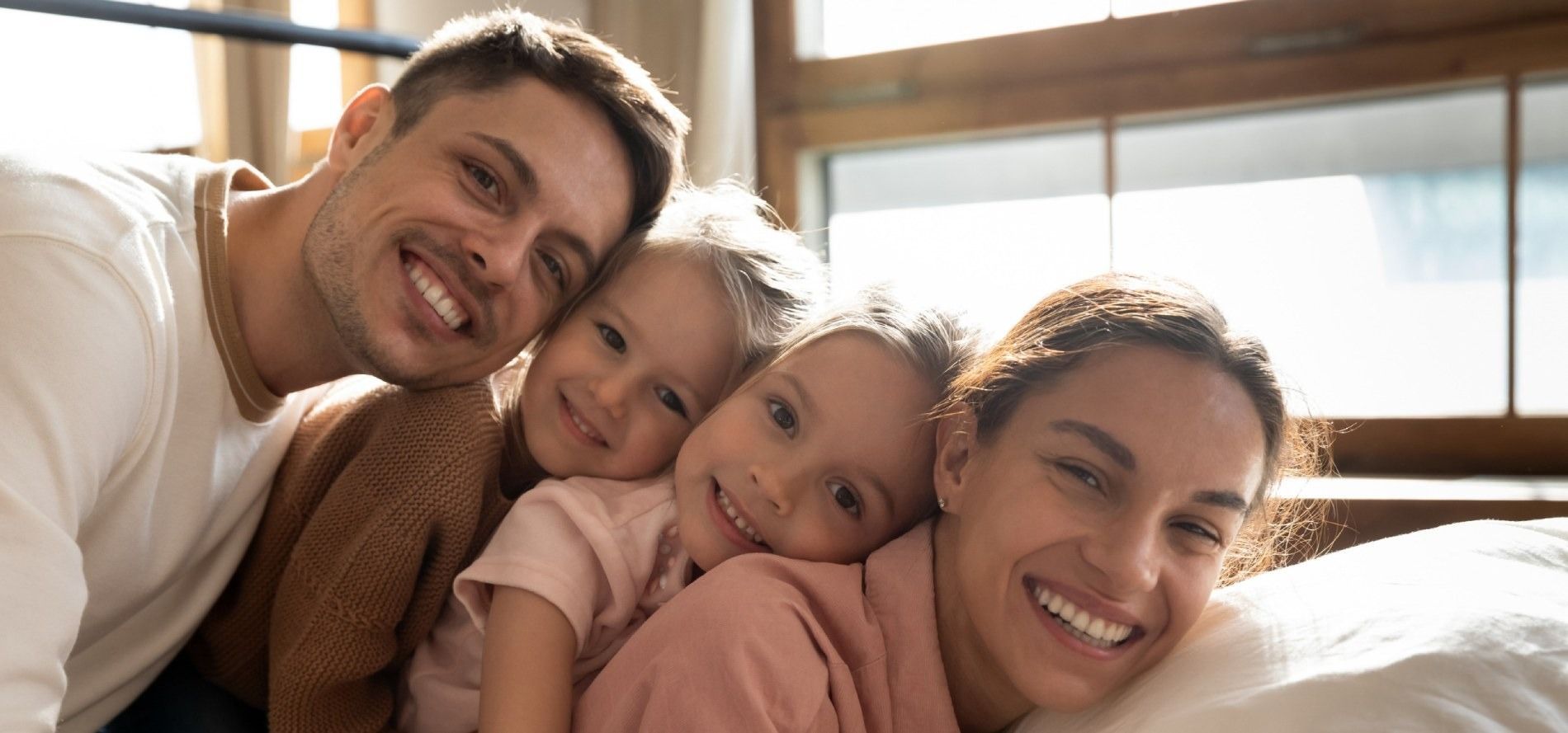 Una familia posa para una fotografía mientras están acostados en una cama.