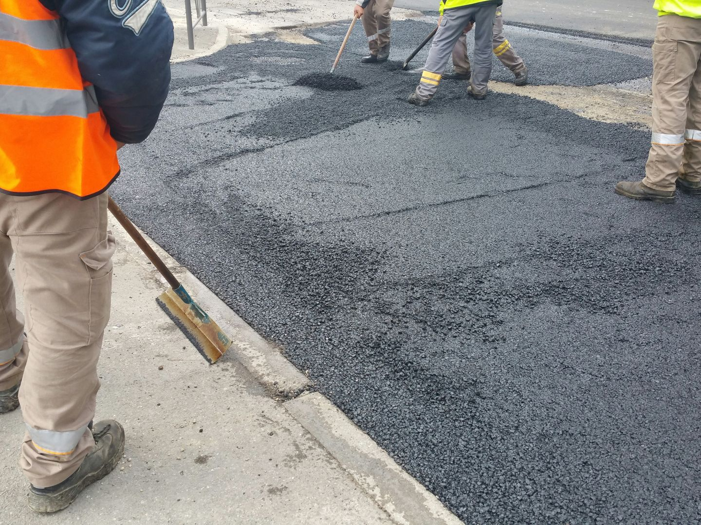 Des ouvriers utilisent des râteaux pour étaler et niveler l'asphalte noir fraîchement posé sur une rue.