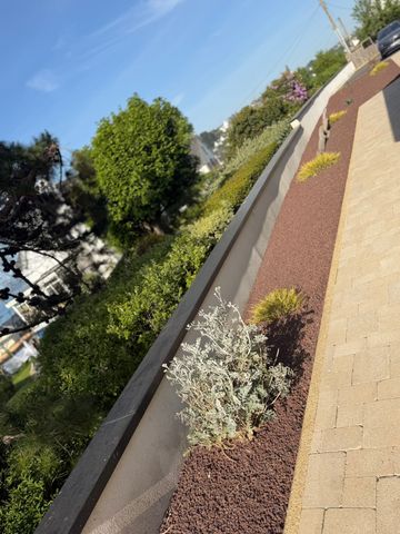 Une maison blanche avec un toit de tuiles, une allée de gravier et divers arbustes et arbres dans la cour avant.