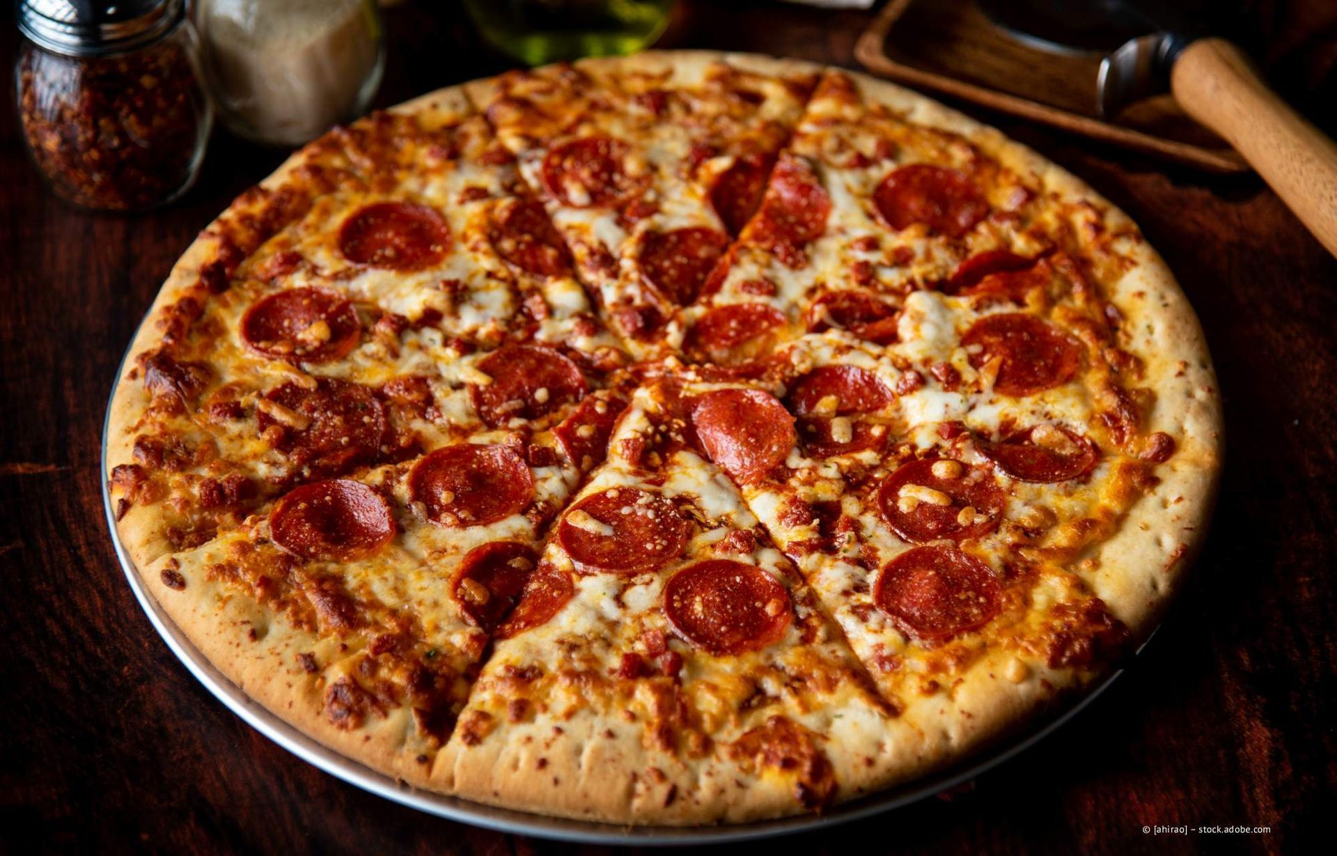Pepperoni-Pizza auf einem Backblech, mit geschnittenen Stücken und einem Holztisch im Hintergrund