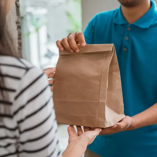 Un hombre con una camisa azul le da una bolsa de papel marrón a una mujer.
